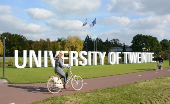 Fietsers fietsen langs Universiteit of Twente letters